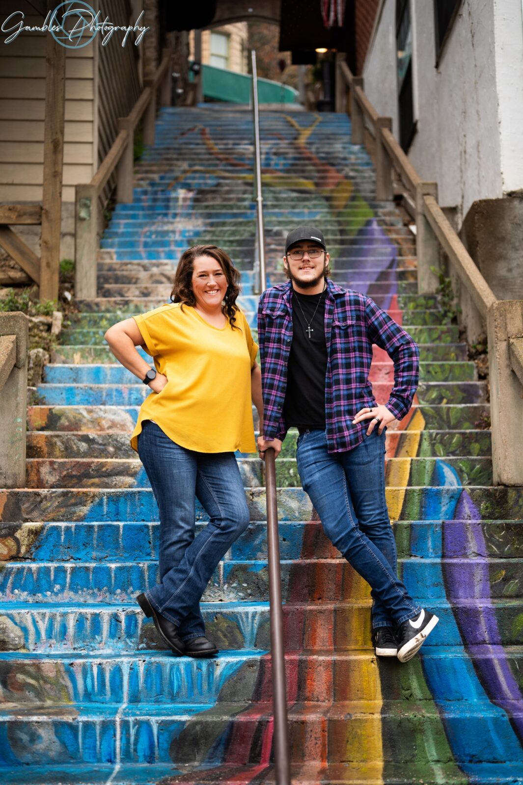 Hands on opposing hips, a man and woman stand and smile on the Rainbow Stairs of Eureka Springs, AR. Photo by Gambles Photography