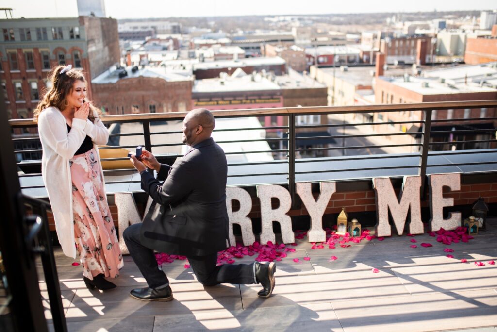 Down on one knee and the cityscape of Springfield, MO behind him, a man proposes at Vantage Rooftop. Photo by Gambles Photography