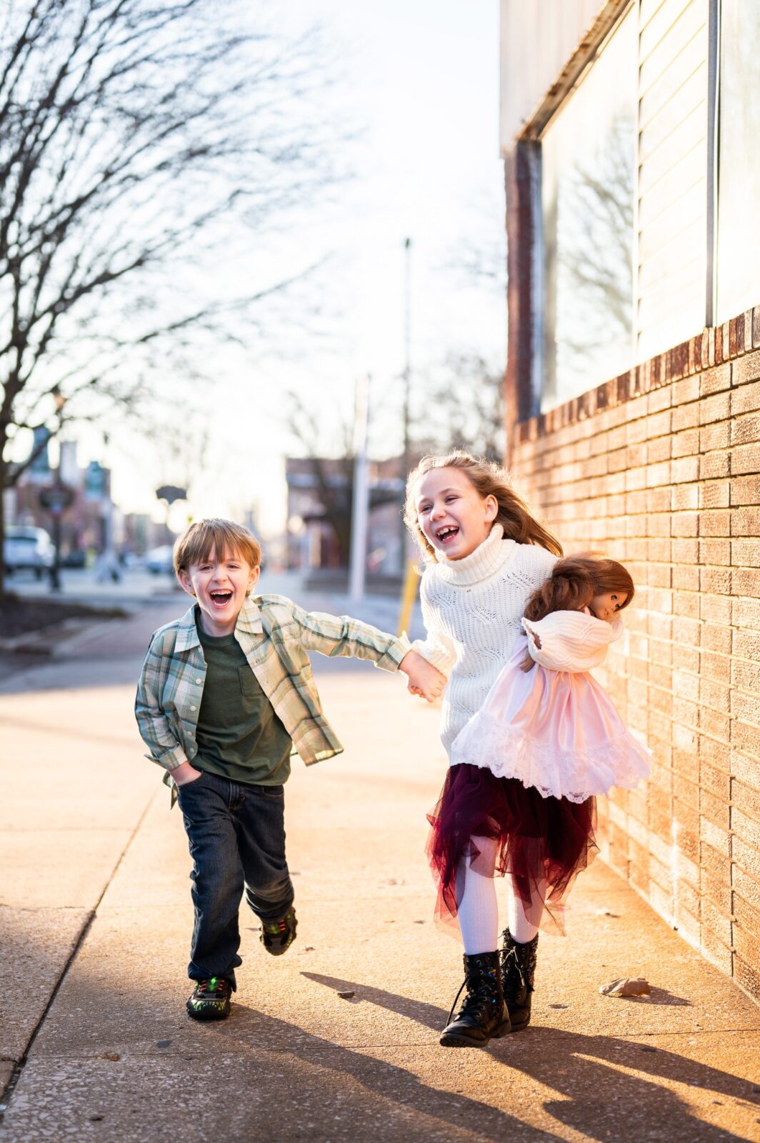 Siblings hold hands, smiling and laughing as they run down the concrete streets of Historic Commercial Street in Springfield, MO. 