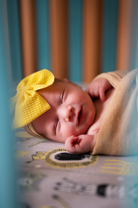 with a yellow bow on, a newborn sleeps quietly in her crib during infant photos in Springfield, MO