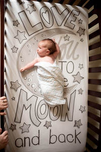 sleeping in a crib with sheets that say 'I love you to the moon and back", a baby is photographed during a newborn photoshoot by Gambles Photography