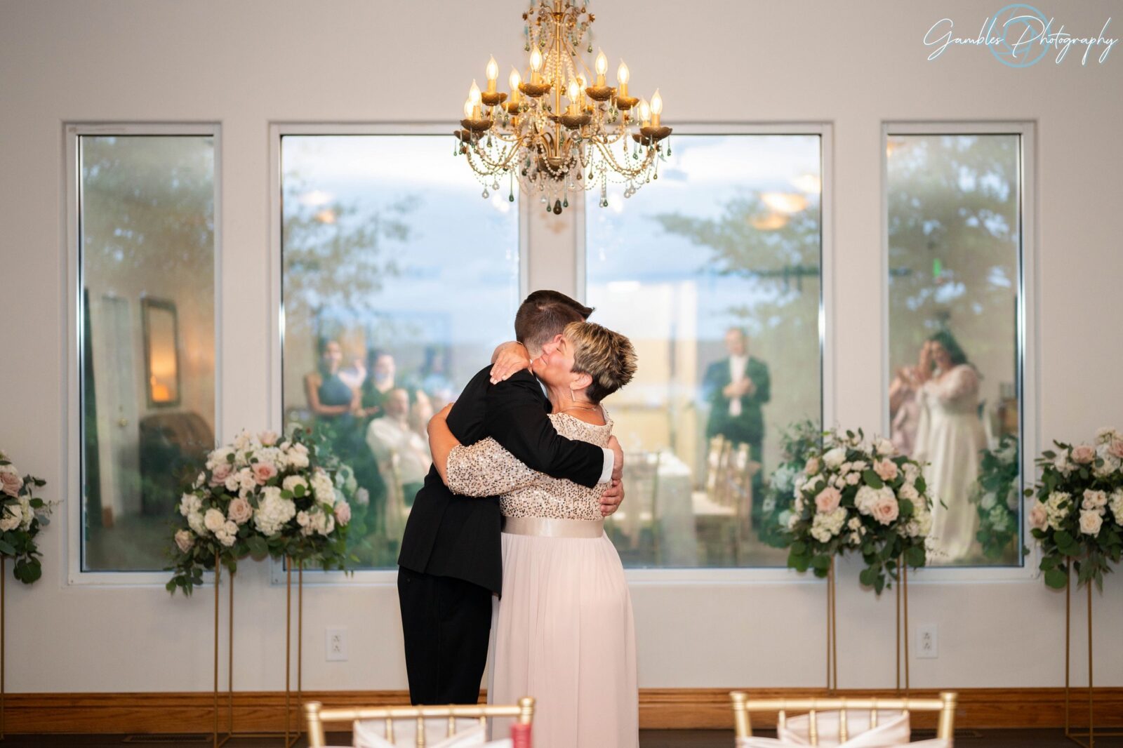 A wedding party watches the mother of the groom and the groom embrace during a small wedding in Branson, MO. Wedding photography by Gambles Photography