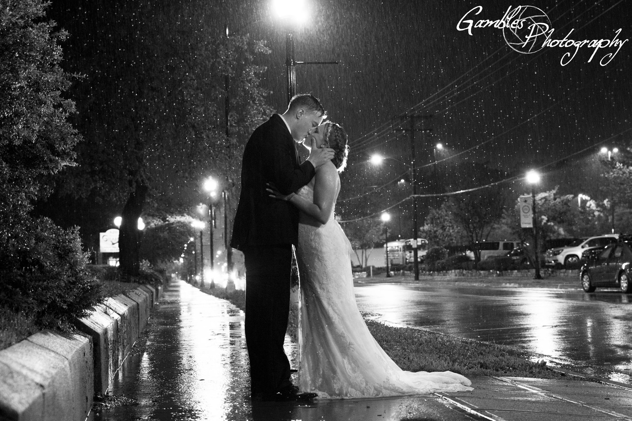 on their wedding night, a couple kisses in the rain after their wedding in Downtown Springfield, MO. Photo by Gambles Photography