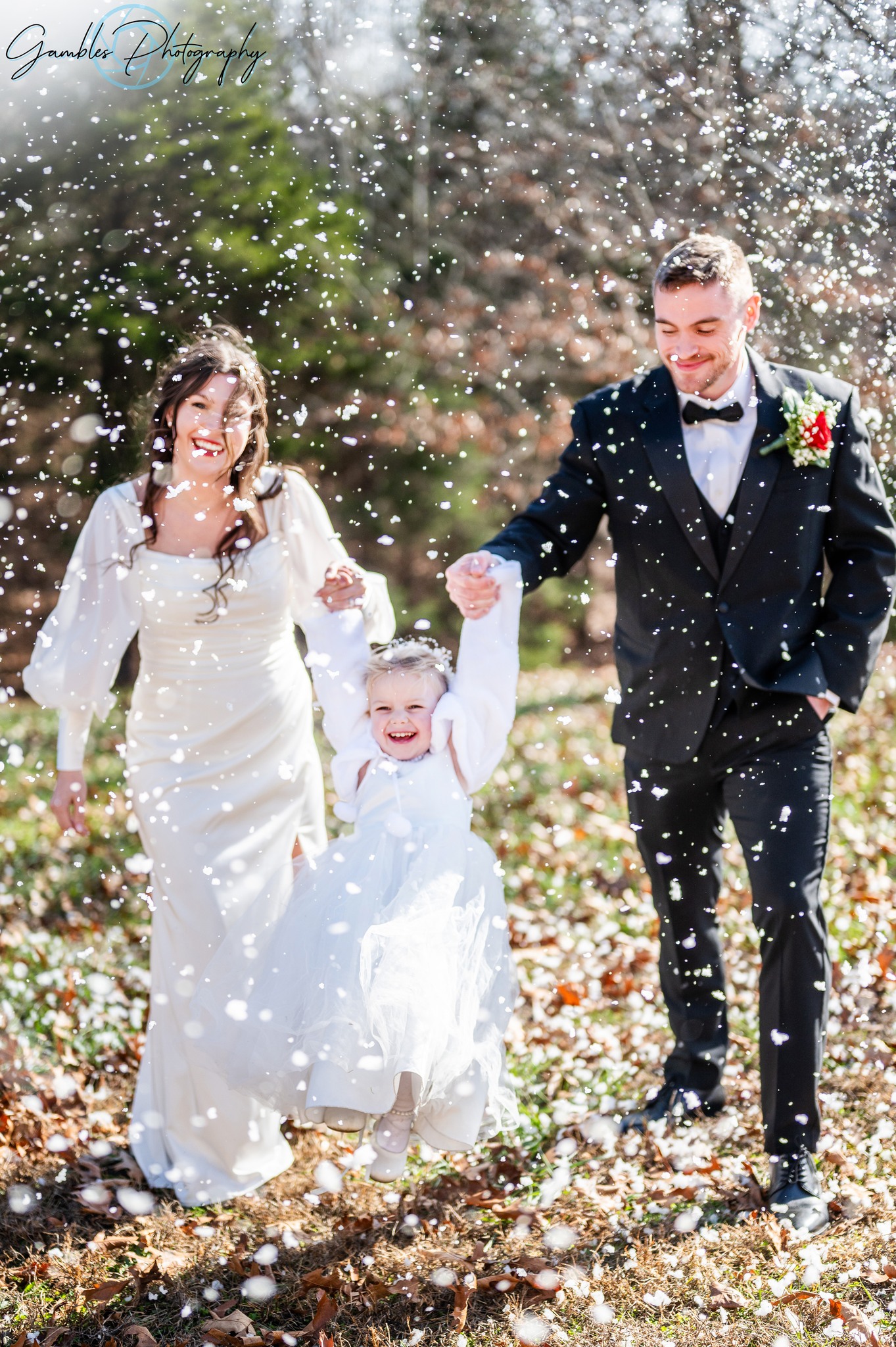 a couple holds each of their daughters hands while it snows on their wedding day. Photo by Gambles Photography